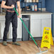 A man using a Lavex green threaded fiberglass broom handle in a hospital cafeteria.