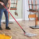 A man using a Lavex red metal mop handle to mop the floor in a professional kitchen.