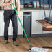 A man in a professional kitchen using a green Lavex mop handle.