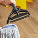 A hand using a Lavex blue fiberglass mop handle to clean a floor.