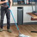 A man using a Lavex blue fiberglass mop handle to clean the floor in a professional kitchen.