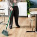 A man using a Lavex green fiberglass broom handle to sweep the floor in a corporate office cafeteria.