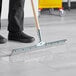 A person using a Lavex rubber floor squeegee with a metal frame to clean a white floor.