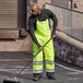 A person in Cordova Hi-Vis Lime quilted bib pants sweeping a parking lot.
