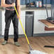 A man using a Lavex yellow fiberglass mop handle to mop a floor in a professional kitchen.