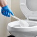 A person in blue gloves cleaning a toilet with a Lavex white acrylic yarn toilet bowl brush.