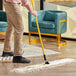 A person using a Lavex yellow metal mop handle to mop a floor.