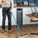 A man using a Lavex blue threaded fiberglass broom handle to sweep the floor in a professional kitchen.