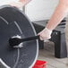 A person holding a Choice black nylon utility brush and cleaning a black bucket.