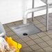 A Regency stainless steel floor sink with a drain and a mop bucket next to it.