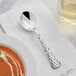 A Visions silver plastic soup spoon on a napkin next to a bowl of soup.