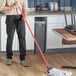 A man using a Lavex red metal mop handle to clean the floor in a professional kitchen.