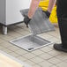 A person in black gloves holding a Regency stainless steel metal grate over a drain.