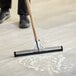 A person using a Lavex black double neoprene foam floor squeegee with metal frame to clean the floor.