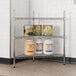 A metal Regency wire shelf with three levels of jars of food.