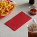 A basket of french fries and a red napkin on a table with a drink.