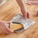 A hand holding a piece of cheese in a Lavex foil wrapper.