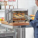 A woman wearing gloves places oranges in an Avantco stainless steel food dehydrator.