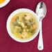 A white Carlisle Dallas Ware bouillon bowl filled with soup, meatballs, and vegetables with a spoon next to it.