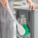 A woman using a Lavex green floating utility brush to clean a metal surface.