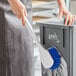 A woman cleaning a trash can with a Lavex blue utility brush.