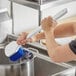 A person cleaning a pot with a Lavex blue polyester scrub brush.