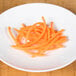 A pile of julienne-cut orange carrots on a wood surface.