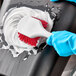 A person in blue gloves using a Lavex red pot scrub brush to clean a black surface.