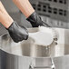 A person wearing black gloves using a Lavex white utility brush to clean a large pot.