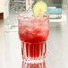 A Libbey highball glass with a red drink and ice, with a lime slice on the rim.