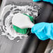 A person using a Lavex green polyester pot scrub brush to clean a black surface.