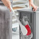 A person cleaning a trash can with a Lavex red utility brush.