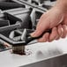 A hand using a black Lavex toothbrush style grout brush with stainless steel bristles to clean a stove.