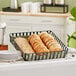 A black square iron powder-coated basket holding food on a bakery counter.