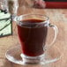 A glass cup of Ellis Donut Shop Blend coffee on a saucer.