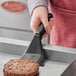 A person using a Fourt&#233; black nylon solid turner to flip a burger on a pan.
