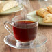 A glass cup of Ellis Mezzaroma Sugar Cookie coffee on a saucer with a plate of pastries.