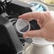 A hand placing an Ellis Presidential coffee single serve cup into a coffee maker.