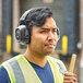 A man wearing Howard Leight by Honeywell Verishield earmuffs and a yellow vest holding a hammer.