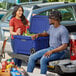 A man and woman sitting on the back of a truck next to a CaterGator Navy outdoor cooler.