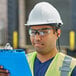 A man wearing a Honeywell white hard hat with ratchet adjustment and safety glasses holding a clipboard.