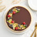 A chocolate tart with berries and gold leaf on a white plate.