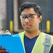 A man wearing Honeywell Uvex safety reader glasses and a safety vest holding a clipboard.
