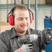 A man wearing Howard Leight red and black earmuffs and gloves using a drill.