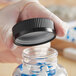 A gloved hand opening a black child resistant 45/400 plastic bottle cap with a heat induction liner.