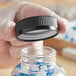 A hand using a black child resistant cap to close a clear jar of pills.