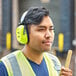 A man wearing Howard Leight Hi-Vis over-the-head earmuffs and a yellow vest using a hammer.