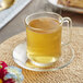 A glass cup of Bigelow Lemon and Echinacea tea on a saucer with a spoon.