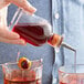A person using an Arcoroc clear bitters bottle to pour liquid into two glasses.