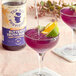 A glass of purple Top Hat Provisions Blue Butterfly Pea Flower drink with fruit and a lime slice.